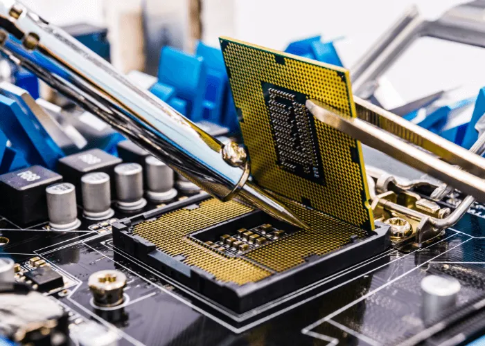Primer plano de unas manos instalando una CPU en una placa base utilizando herramientas, con componentes de hardware informático visibles en el fondo.