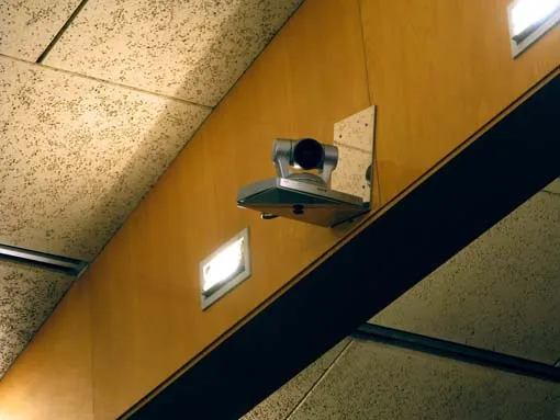Hay una cámara de seguridad montada en un panel de madera cerca del techo, encima de unos fluorescentes.