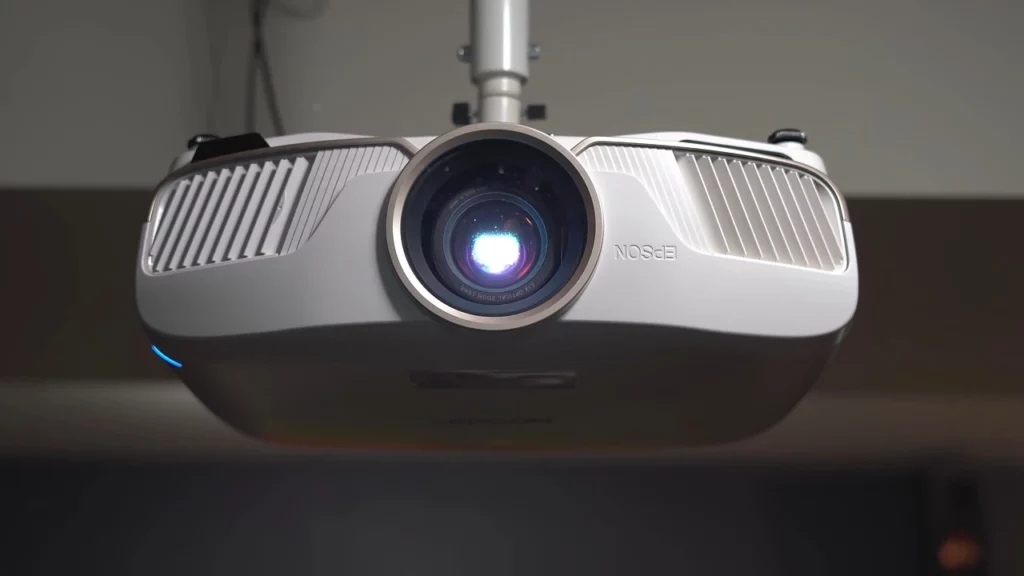 Primer plano de un proyector montado en el techo encendido, con la luz que emite su lente, ideal para instalaciones multimedia y soluciones audiovisuales profesionales.